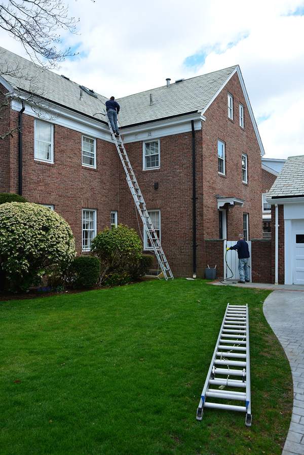 gutterclean-tall-ladder Technician on a tall ladder cleaning a home gutter